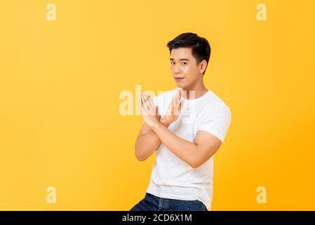 Portrait d’un jeune homme asiatique beau montrant un désaccord geste de la main x croisé sur fond jaune studio isolé Banque D'Images