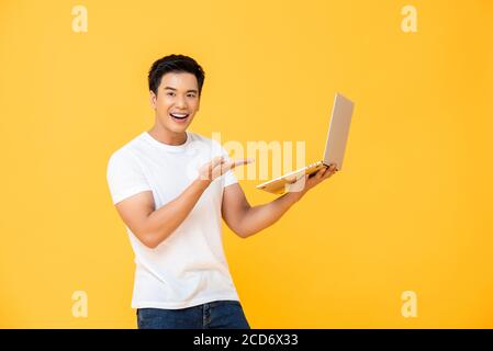 Portrait d'un jeune homme asiatique souriant présentant un ordinateur portable pendant souriant et regardant la caméra sur fond jaune studio isolé Banque D'Images