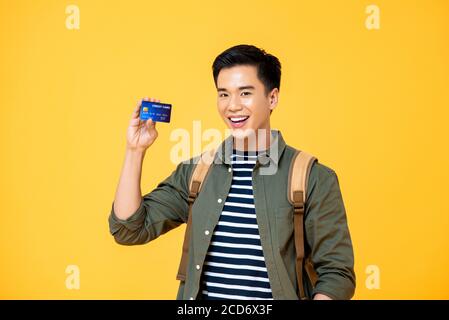 Portrait d'un jeune touriste asiatique souriant en train de faire la démonstration carte de crédit dans un studio isolé de fond jaune Banque D'Images