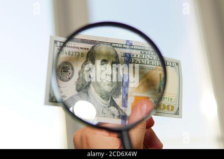 Une facture de cent dollars sous loupe est inspectée Conceptual photo sur fond de fenêtre Banque D'Images