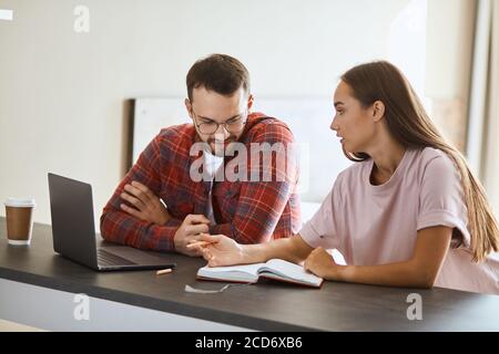 Charmant non enregistré indépendant assis à une table en bois sombre, garde les mains pliées, regarde loin, parlant à une belle femme aux cheveux longs dans un restaurant confortable, côté i Banque D'Images