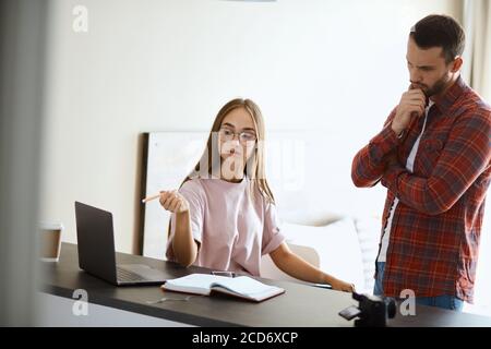 Un jeune petit couple qui pense à des questions d'affaires dans une salle lumineuse, résout des problèmes, exprime son étonnement, prise de vue en intérieur Banque D'Images