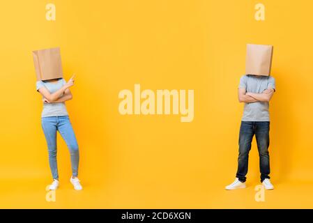 Portrait complet de couple anonyme sans visage couvrant les têtes avec sacs en papier présentant l'espace entre isolé sur fond jaune studio Banque D'Images