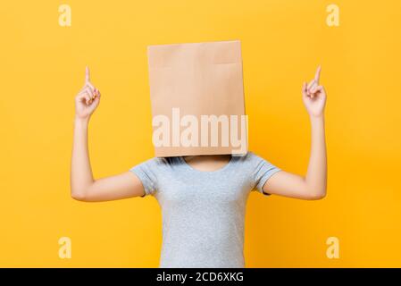 Portrait de concept de la femme anonyme avec la tête couverte de papier sac pointant les deux doigts vers le haut sur fond jaune studio Banque D'Images