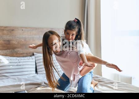 Jolie petite fille charmante sur une balade à dos piquant avec une belle jeune maman, regardant l'appareil photo avec le visage calme, femme avec les cheveux longs jouant avec l'enfant Banque D'Images