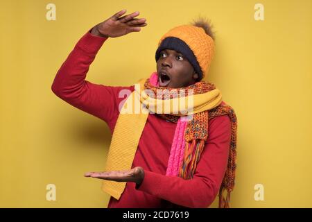 Homme africain en vêtements chauds en montrant avec les mains grandes la taille se sent choquée Banque D'Images