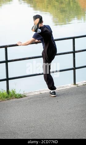 Un homme américain asiatique remarquablement flexible s'enferme pour les exercices du matin en donnant un coup de pied très haut à la jambe. À Kissena Park, Flushing, Queens, New York . Banque D'Images