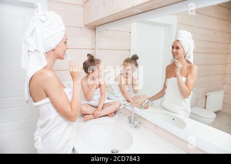 Une famille heureuse se brossant les dents et passant du temps ensemble. Mère et sa fille enfant fille embrassant et embrassant dans la salle de bains blanche. Femme et Banque D'Images