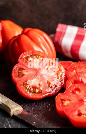 Tomatoe rouge en tranches de beefsteak sur une table noire. Banque D'Images