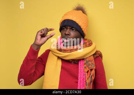 Homme africain déçu en vêtements d'hiver montrant de petite taille. Banque D'Images