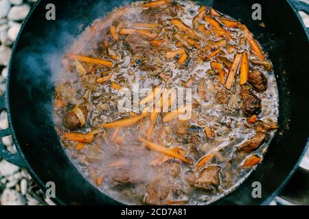 Gros plan de la surface du pilaf fini dans un chaudron au feu. Orange les grosses carottes et la viande sont mijotés à haute température. Banque D'Images