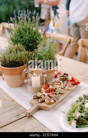 Planche à découper en bois avec des coupures de froid sur la table près des pots de fleurs et une bougie dans une fiole. Banque D'Images