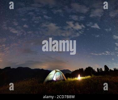 Tente éclairée et feu de camp sous un ciel étoilé incroyable, soirée d'été dans les montagnes, beauté de la nature. Camping de nuit Banque D'Images