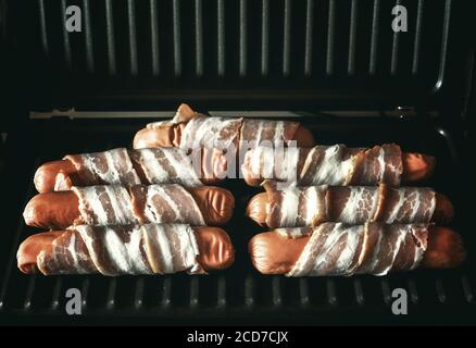 Les saucisses appétissantes enveloppées de bacon sont grillées sur un appareil électrique gril Banque D'Images