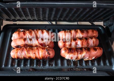 Les saucisses appétissantes enveloppées de bacon sont grillées sur un appareil électrique gril Banque D'Images