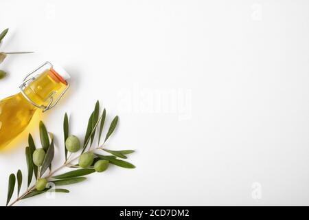 Bouteille de verre et branche d'olive pleine d'olives sur table blanche. Vue de dessus. Banque D'Images