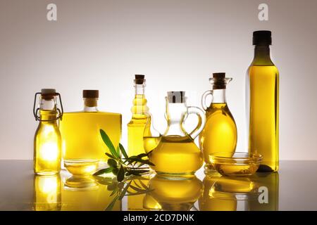Récipients en verre remplis d'huile d'olive rétro-éclairé sur table en verre et fond gris dégradé isolé. Vue avant. Banque D'Images