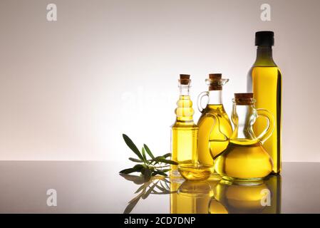 Récipients en verre remplis d'huile d'olive rétro-éclairé sur table en verre et fond gris dégradé isolé. Composition à droite avec espace pour le texte. Banque D'Images