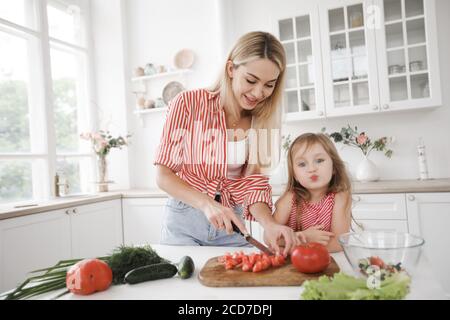 Une petite fille mignonne et sa belle mère cuisent le dîner dans la cuisine à la maison blanche Banque D'Images