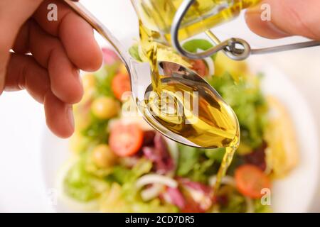 Personne versant l'huile d'une bouteille d'huile en verre sur une cuillère pour habiller la salade. Vue de dessus Banque D'Images