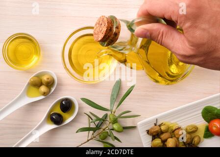 Différentes variantes d'olives à manger et d'huile dans des récipients sur banc de cuisine en bois et bol en verre pour les mains. Vue de dessus. Banque D'Images
