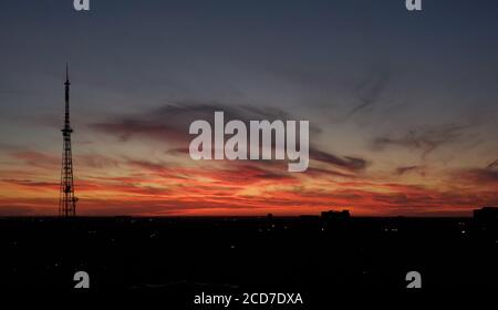 Coucher de soleil à couper le souffle sur la ligne d'horizon urbaine avec silhouette de tour de communication. Nuages rouges violets sur fond bleu foncé Banque D'Images