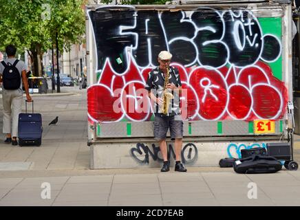 Londres, Angleterre, Royaume-Uni. Busker jouant le saxophone devant le graffiti à Oxford Street Banque D'Images