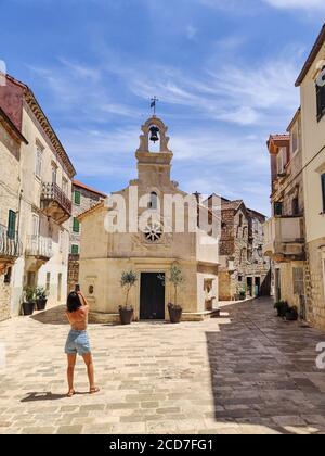 Femme touriste prenant photo de l'église de centre commercial sur la place du petit village urbain de Stari grad sur l'île de Hvar en Croatie, Mer Adriatique, Europe Banque D'Images
