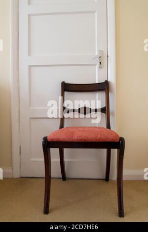 Chaise de salle à manger tenant une porte fermée dans une chambre dans une maison de banlieue, Londres, Angleterre, Royaume-Uni Banque D'Images