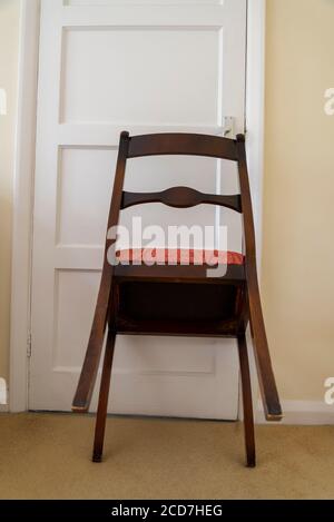 Chaise de salle à manger tenant une porte fermée dans une chambre dans une maison de banlieue, Londres, Angleterre, Royaume-Uni Banque D'Images