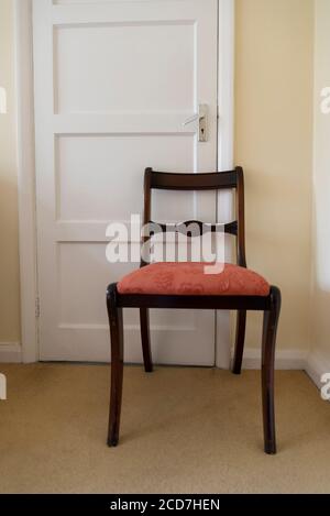 Chaise de salle à manger tenant une porte fermée dans une chambre dans une maison de banlieue, Londres, Angleterre, Royaume-Uni Banque D'Images