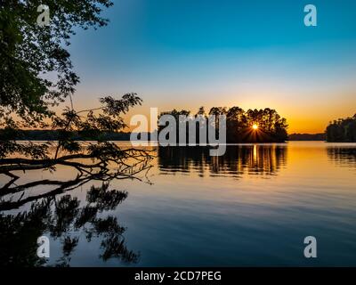 Coucher de soleil sur le lac Pymatuning en Pennsylvanie à la fin de l'été. Un arbre tombé au premier plan et le soleil éclate à travers les arbres sur un isl Banque D'Images