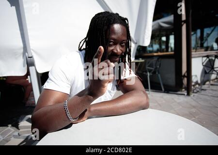 Portrait d'un Africain, cheveux longs, dreadlocks, il rit et pointe un doigt, jour d'été, à l'extérieur. Photo de haute qualité Banque D'Images