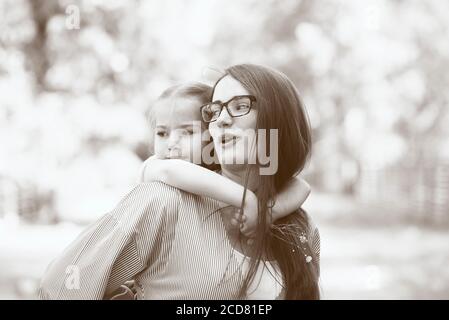 Bonne petite fille assise sur les épaules de sa mère ou de retour sur une journée ensoleillée d'été, portrait en sépia Banque D'Images