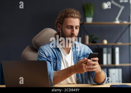 Jeune homme en utilisant un smartphone et souriant. Un homme d'affaires heureux utilisant des applications de téléphonie mobile, des SMS, naviguer sur Internet, regarder smartphone. Concept Banque D'Images