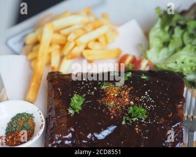 Côtes de porc grillées à la sauce barbecue et caramélisées Miel avec en-cas de frites sur une assiette en bois Banque D'Images