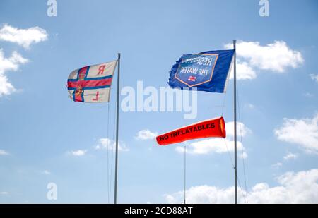 Les drapeaux RNLI, « No Inflatables » et « respect de l'eau » flottent dans le vent avec un ciel bue et un nuage clair en arrière-plan. Banque D'Images