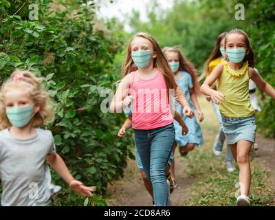 Joyeux petits enfants portant un masque de protection pour sauter et courir sur la prairie, forêt. Semble heureux, gai, sincère. CopySpace. Enfance, pandémie concept. Soins de santé, pandémie de coronavirus. Banque D'Images