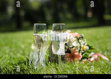 Deux verres de champagne de mariage sont sur l'herbe, sur fond de bouquet de mariage. Jour ensoleillé. Gros plan Banque D'Images