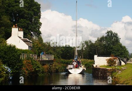 Un yacht sur le canal de Crinan juste en passant par le Passerelle de balancement Crinan avec une famille à bord et Crinan Maison de pont et l'opérateur de pont Banque D'Images