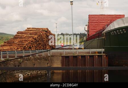 Vue sur le quai d'Ardrisciig, Argyll, en Écosse, d'une grande pile de bois et de la commission forestière attendant d'être expédiée sur un grand bateau Timber Link Banque D'Images