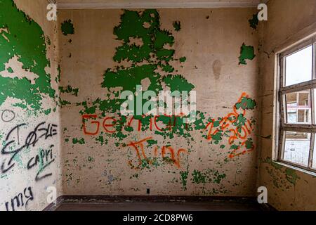 La peinture verte écaillée révèle les couches sous-jacentes au coin d'une pièce abandonnée du Sanatorio Durán près de Tierra Blanca, Costa Rica, des tags graffiti orange recouvrent le mur. Banque D'Images