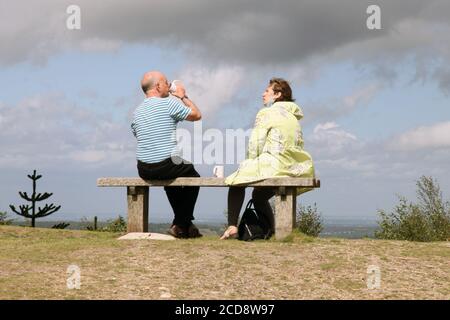 Couple d'âge mûr assis de derrière en admirant la vue depuis Leith Hill, site du National Trust buvant des tasses de chine pour réduire la litière, 2020 Banque D'Images