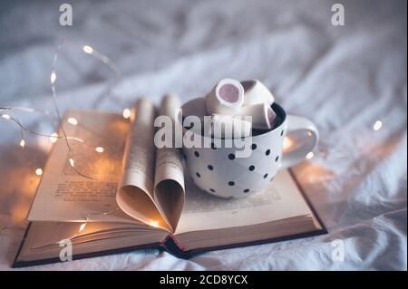 Tasse de café avec guimauve sur livre ouvert avec coeur en forme de pages pliées gros plan. Saison d'hiver.