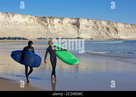 Maroc, Sahara occidental, Dakhla, deux surfeurs marocains avec leurs planches sur la plage d'Araiche bordée d'une falaise Banque D'Images