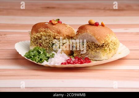 Le Dabeli est un en-cas indien servi avec des graines de grenade et du Cilantro dans une assiette en papier blanc. Sur fond de bois Banque D'Images