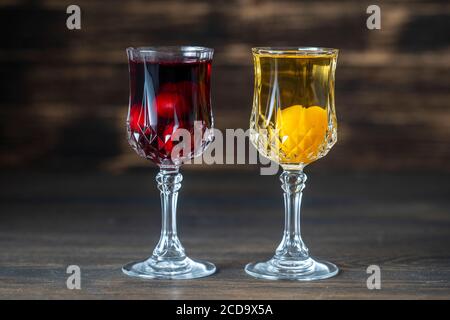 Teinture maison de cerise rouge et de prune de cerise jaune dans des verres de cristal de vin sur fond de bois, Ukraine, gros plan. Fruits boissons alcoolisées conce Banque D'Images