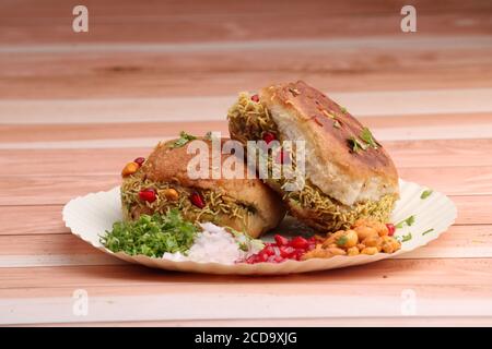 Le Dabeli est un en-cas indien servi avec des graines de grenade et du Cilantro dans une assiette en papier blanc. Sur fond de bois Banque D'Images