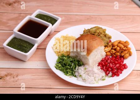 Le Dabeli est un en-cas indien servi avec des graines de grenade et de la coriandre dans une assiette en céramique blanche. Avec chutney vert et chutney de tamarin. Banque D'Images