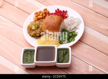 Le Dabeli est un en-cas indien servi avec des graines de grenade et de la coriandre dans une assiette en céramique blanche. Avec chutney vert et chutney de tamarin. Banque D'Images